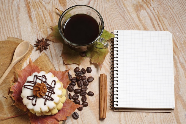 Cup of coffee, small round cake and notebook on old wooden background