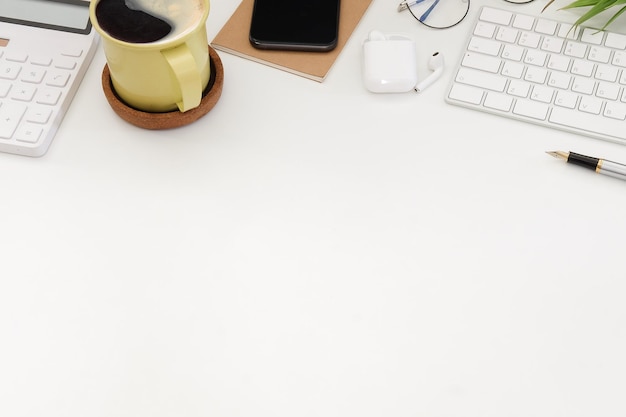 白いオフィスの机の上のコーヒースマートフォン電卓とワイヤレスキーボードのカップ