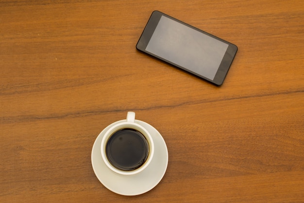 Cup of coffee and smartphone on wooden table. Top view