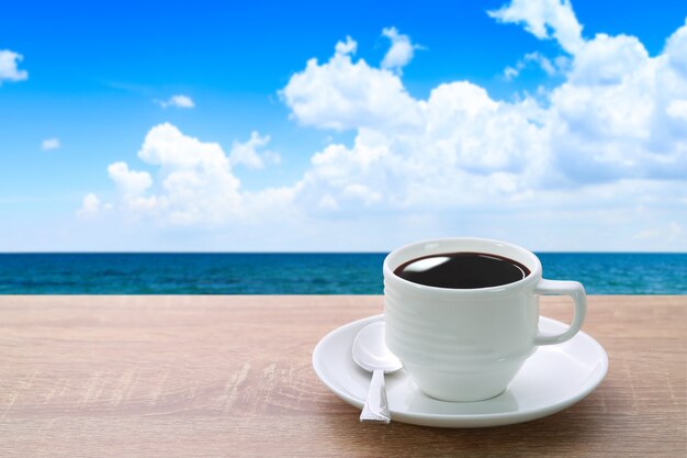 Foto una tazza di caffè e un cucchiaio sullo scrittorio di legno con la bella spiaggia