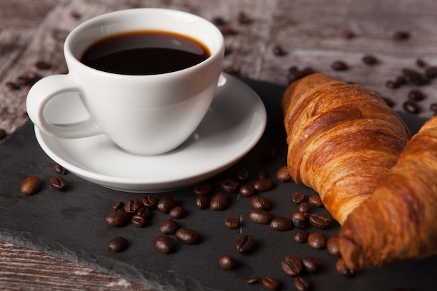 Cup of coffee and spreaded coffee beans with fresh croissants. Delicous dessert.