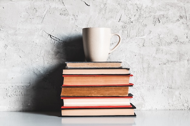 Una tazza di caffè su una pila di libri su sfondo grigio. educazione, studio, hobby, lettura