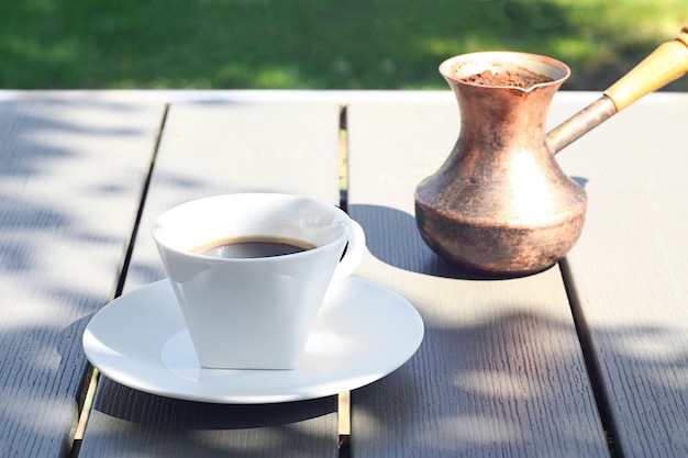 A cup of coffee stands on a wooden table in the garden Behind is a Turk with freshly brewed coffee