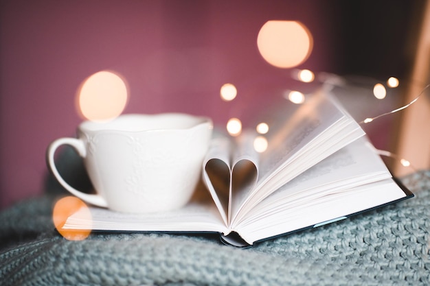 Tazza di caffè che resta sul primo piano del libro aperto sopra le luci. buon giorno.