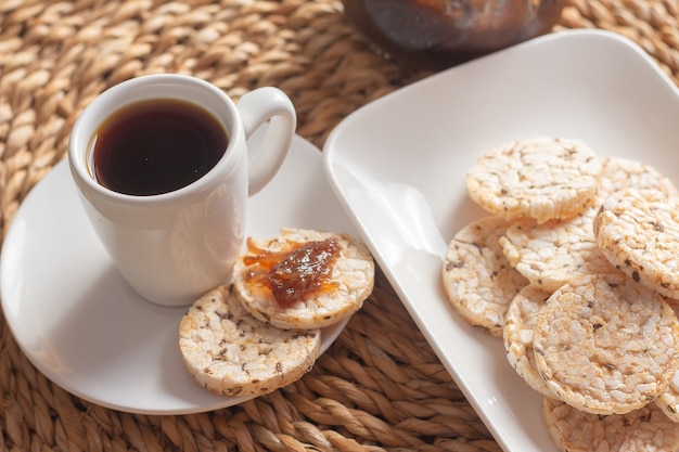 Photo a cup of coffee under the straw table surrounded by a bowl full of rice cookies and a jelly pot