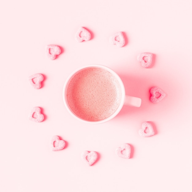 Cup of coffee and sugar hearts on a pink pastel background.