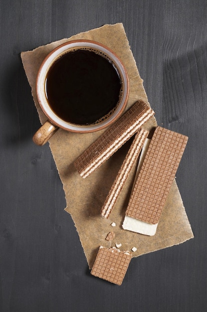 Cup of coffee and sweet chocolate waffles on black wooden background, top view