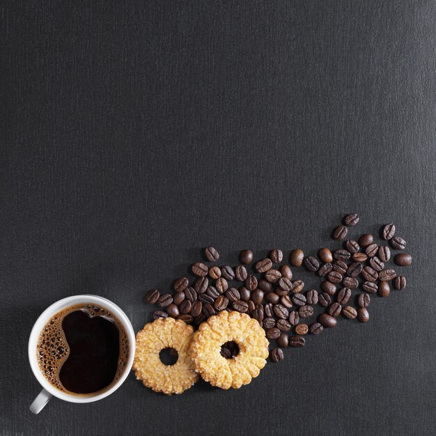 Cup of coffee and sweet shortbread cookies on black stone background, top view with space for text