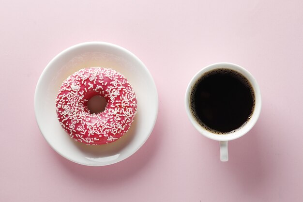 Cup of coffee and sweet tasty donut on a pink background with place for text.