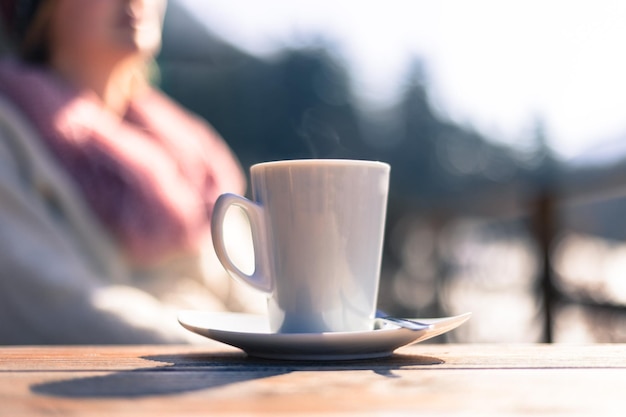 晴れた日の午後に屋外のカフェのテーブルの上のコーヒー カップぼやけた背景の女性