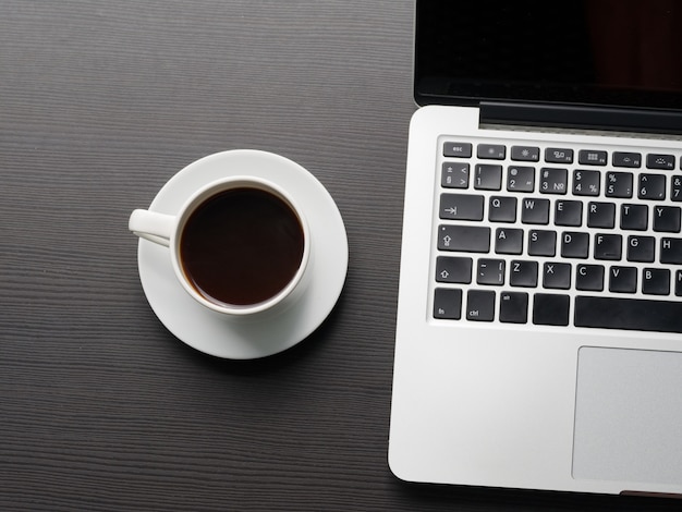 Cup of coffee on the table and laptop computer. top view.