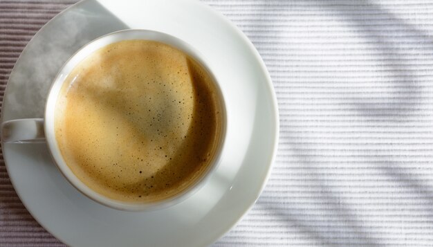 Cup of coffee on a table near the window. Shadows from the window frame