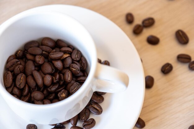 Cup of coffee that full of coffee beans on wooden background with rim light