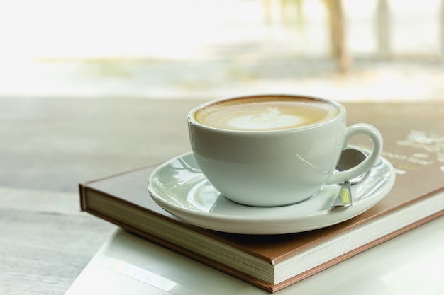 Cup of coffee on top of book and laptop on wooden table in the morning.