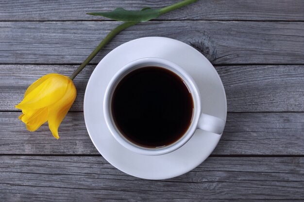 Cup of coffee and tulip flower on wooden background, high angle shot