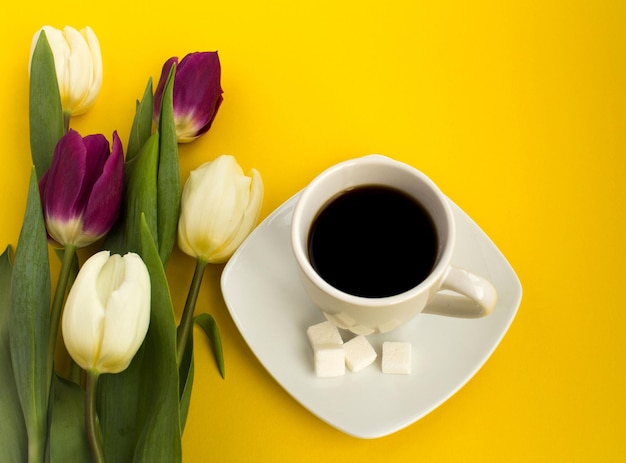 Cup of coffee and tulips on the yellow background. top view