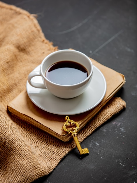 Cup of coffee, and vintage book with key on a dark table