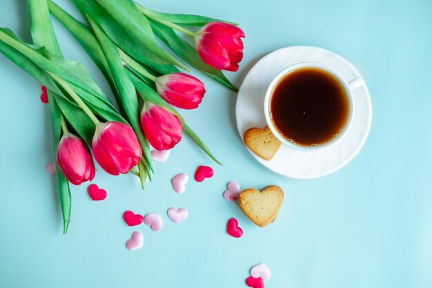 A cup of coffee in a white cup with scattered hearts and red tulips on a blue background