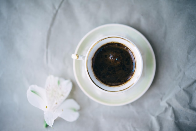 cup of coffee and white flower on gray background. top view