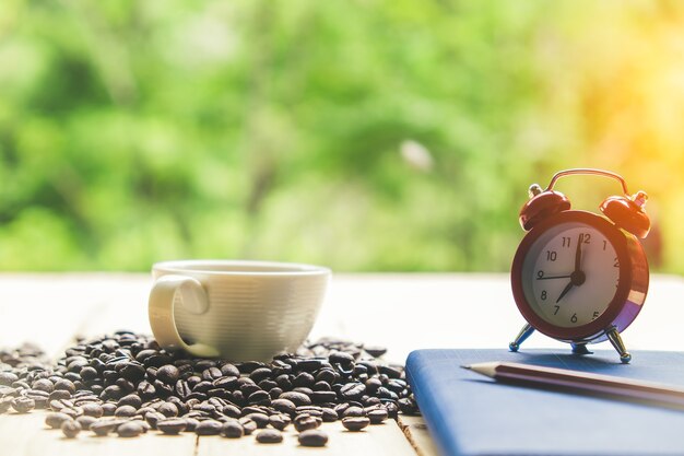 Foto tazza di caffè bianco taccuino, chicchi di caffè e sveglia su un tavolo da tavola di legno.