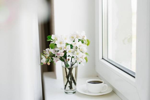 Cup of coffee on a white plate and a vase of flowers on the windowsill Cozy Easter spring still life