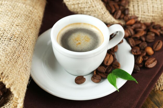 Cup of coffee with beans on table close up