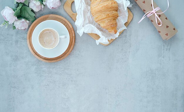 Cup of coffee with bouquet of pink tulips and croissant on white shabby chic background. Valentines, Mothers, Womens Day morning concept. Valentine's day breakfast. Top view. Copy space.