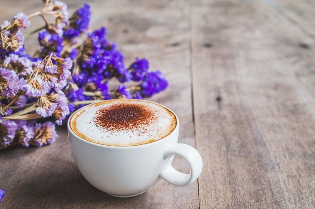 木製の床の背景に紫色の乾燥した花の花束とコーヒーのカップ