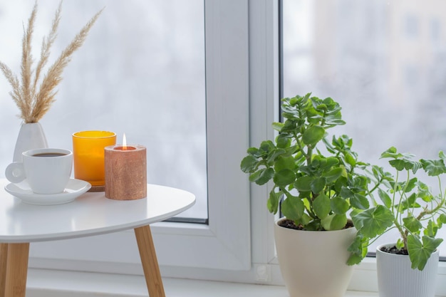 Cup of coffee with burning candles  on white table by window on winter