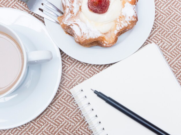 Cup of coffee with cake and notebook