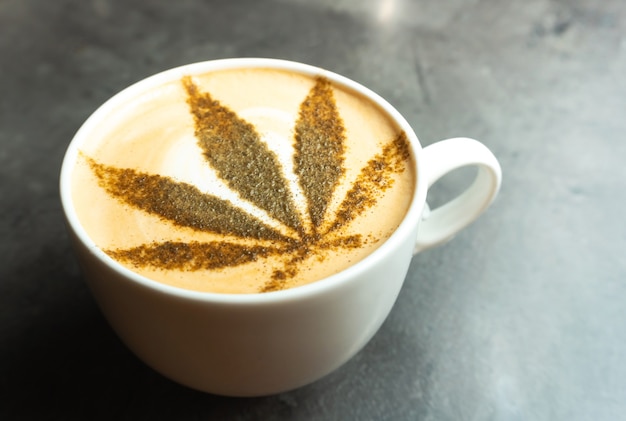 A cup of coffee with cannabis leaf drawn on milk cream.