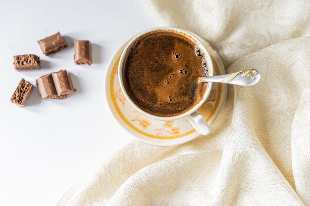 Cup of coffee with chocolate on a light white table and beige napkin Breakfast coffee in bed