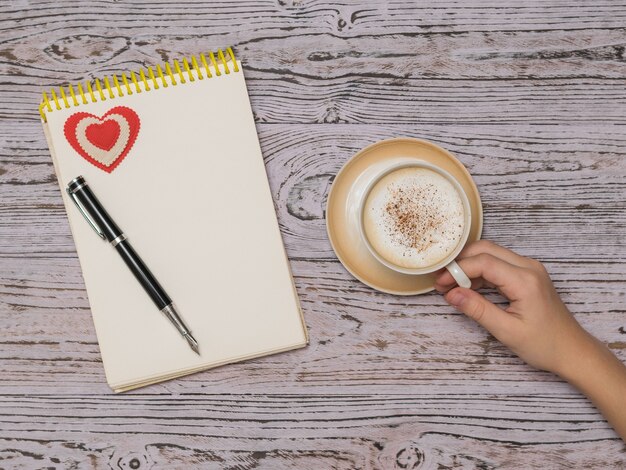 A Cup of coffee with cinnamon and milk and a notebook on a wooden table