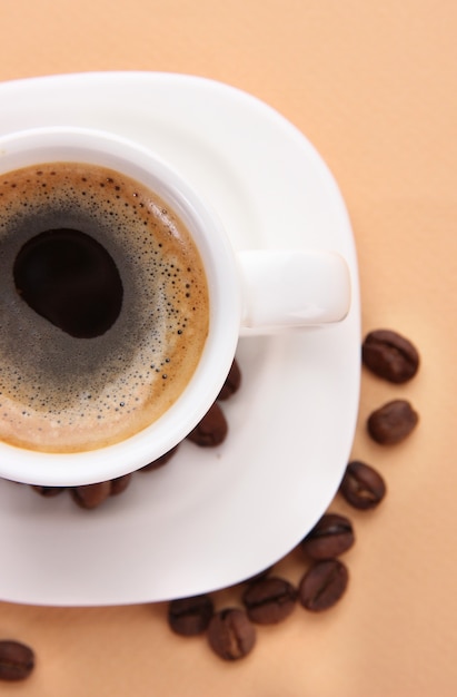 Cup of coffee with coffee beans on beige background