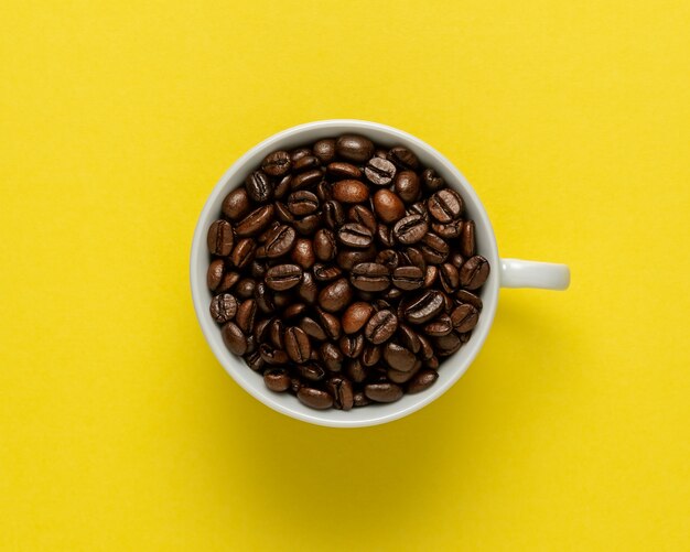 Cup of coffee with coffee beans on yellow background