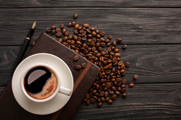 Cup of coffee with coffee grains and notepad on dark boards