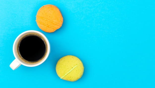 Cup of coffee with colorful macaroons on blue Top view Space for text