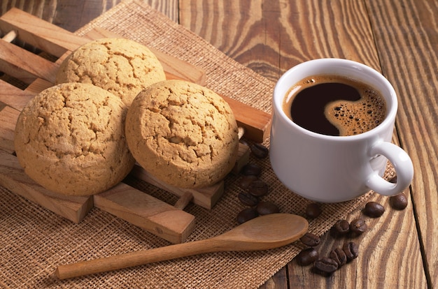 Cup of coffee with cookies on wooden table close up