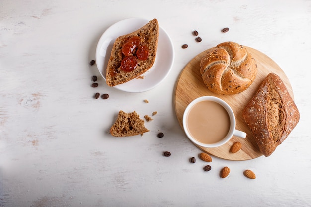 Cup of coffee with cream  and buns on a white wooden background.