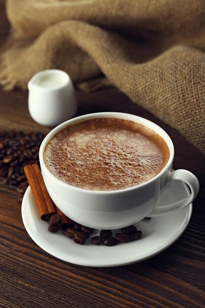 木製の背景にクリームとコーヒー豆とコーヒーのカップ