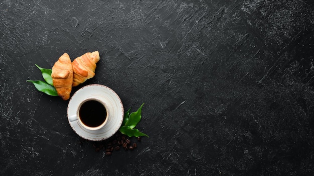 Cup of coffee with croissant. Breakfast. On a black stone background. Top view. Free space for your text.