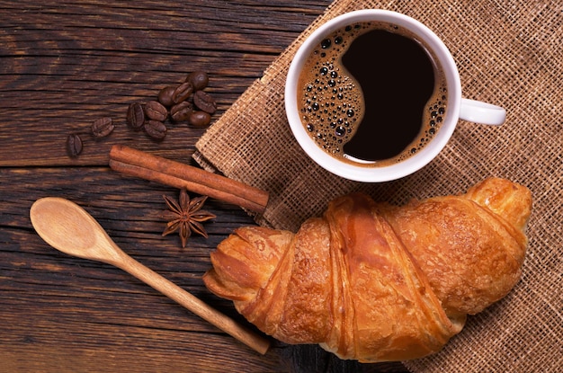 Cup of coffee with croissant on old wooden table top view