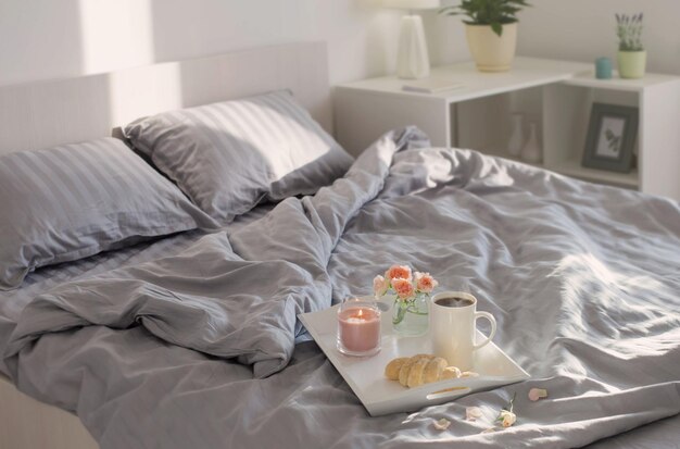 cup of coffee with croissant  and pink roses on bed in  bedroom