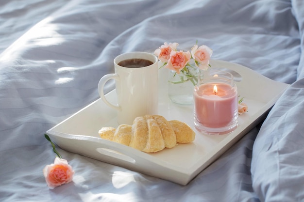 cup of coffee with croissant and pink roses on bed in bedroom