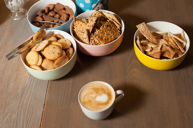 A cup of coffee with dishes with different cookies are on the table