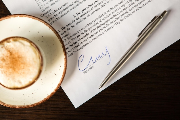 Cup of coffee with foam and cinnamon ballpoint pen and blank contract on a wooden table