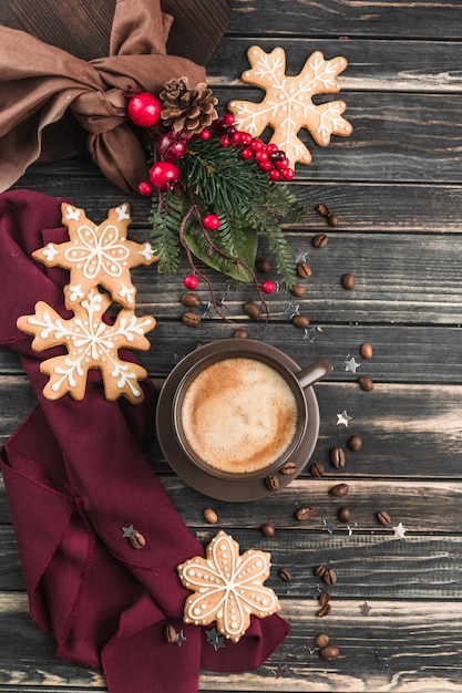 Foto una tazza di caffè con schiuma su un legno scuro con pan di zenzero a forma di fiocchi di neve.