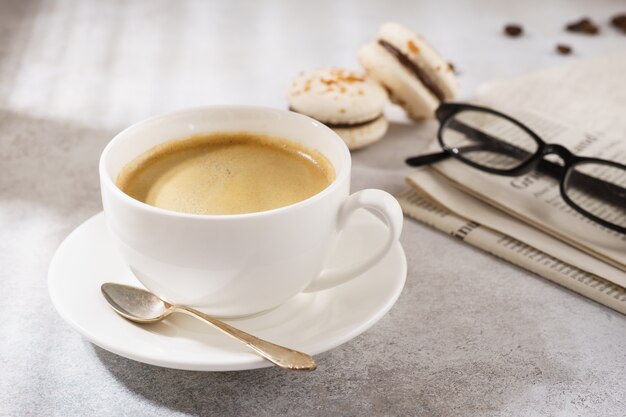 Foto tazza di caffè con macarons francesi, giornali e bicchieri.