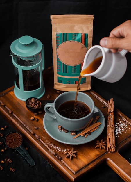 cup of coffee with French press and various unbranded packing on wooden boards and black background