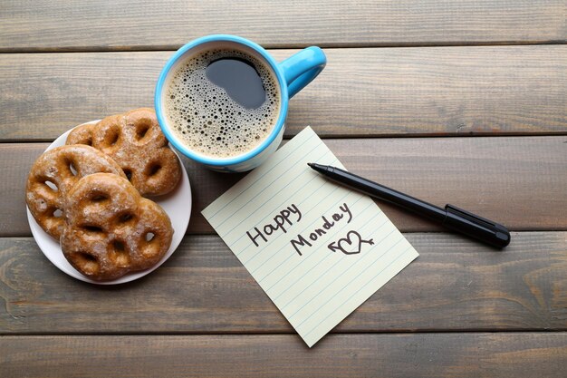 Cup of coffee with fresh cookies and Happy Monday massage on wooden background